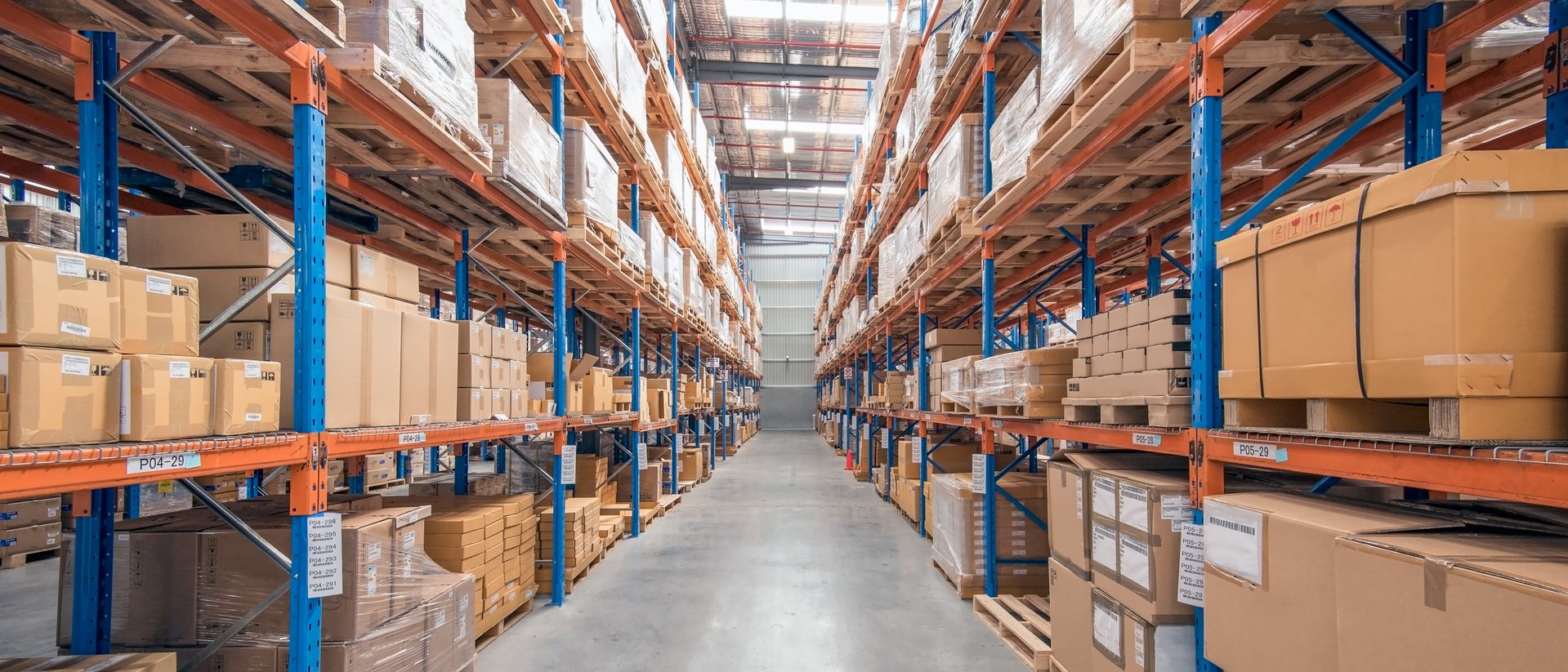 View down an aisle in a warehouse with tall shelves filled with boxes